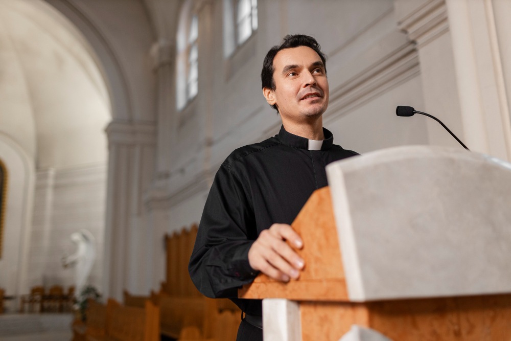 Padre celebrando missa na igreja, usando roupa de padre e falando com uma congregação.