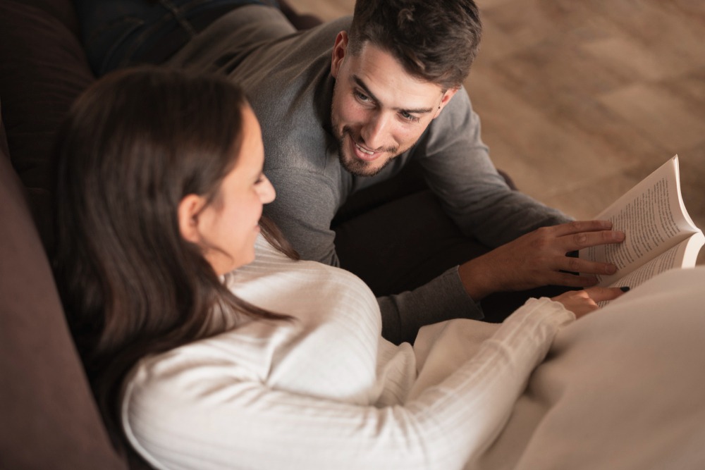 Homem e mulher conversando e lendo um livro juntos em casa, momento de convivência, leitura e troca entre amigos.